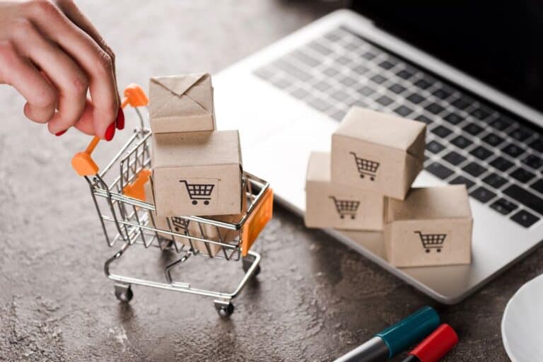 Miniature shopping trolley with small parcels beside a laptop, symbolising the accounting challenges faced by eCommerce companies in managing online orders and inventory.