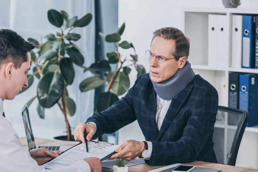 A man in a neck brace reviews legal documents with a professional, discussing his rights after a workplace injury.