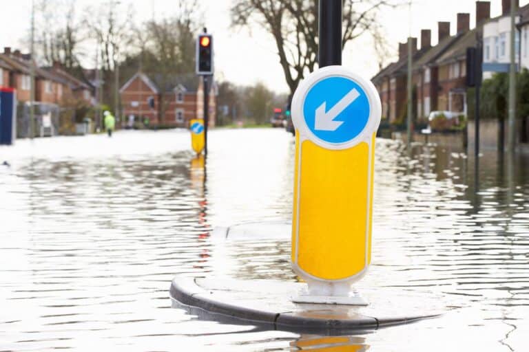 A flooded residential street with a traffic island sign and submerged road, highlighting the impact of natural disasters in a neighbourhood.