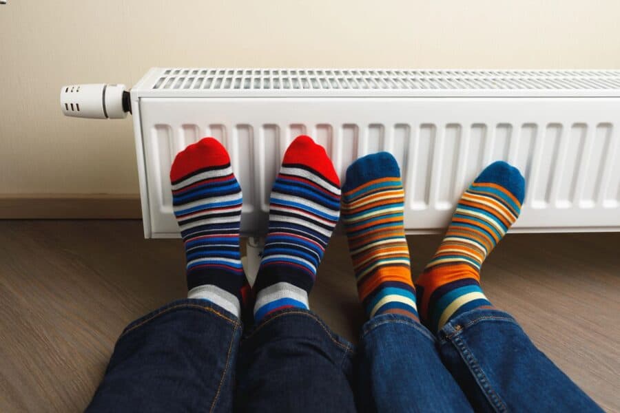 Two pairs of feet wearing colourful striped socks resting against a white radiator, symbolising a cosy way to keep warm during cold weather.