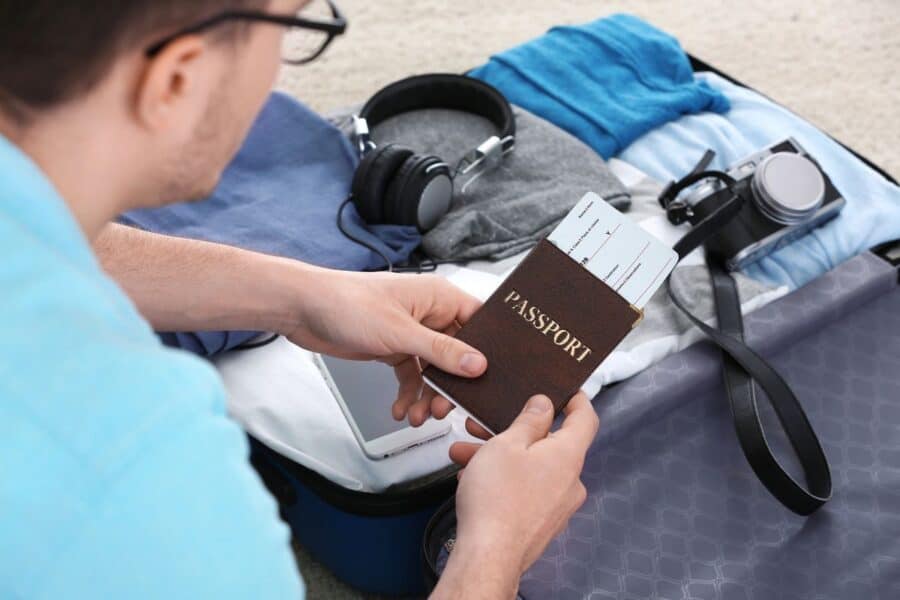 A traveller holding a passport with boarding passes, preparing a suitcase packed with casual clothes, headphones, a camera, and travel essentials,