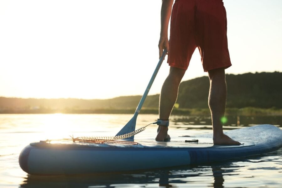 Man wearing swim shorts while stood on a paddle board.