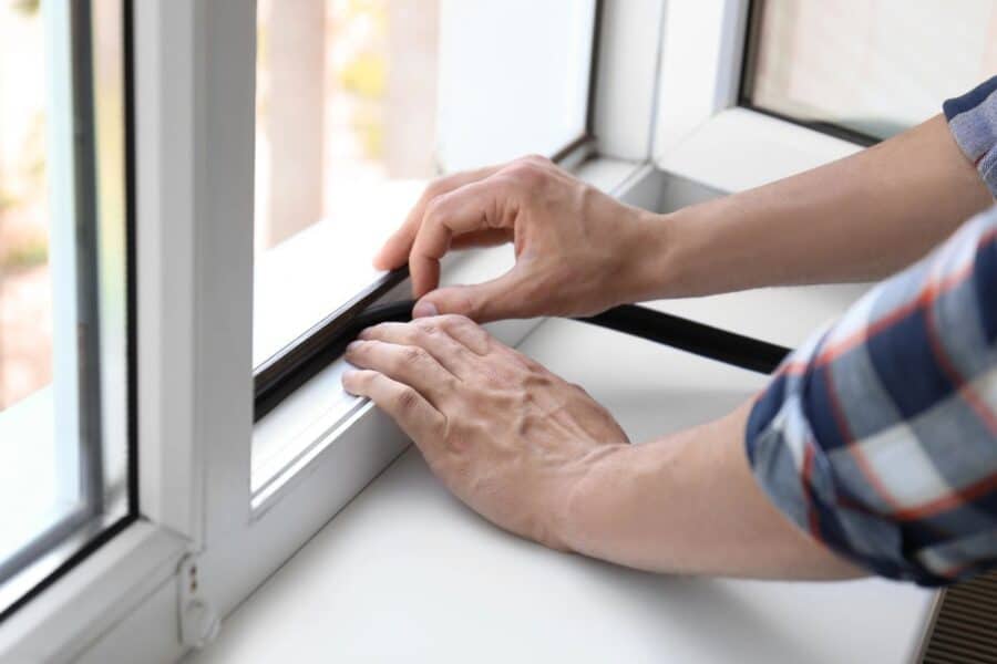 Sealing a window with a rubber strip to prevent drafts, one of the effective ways to keep your house warm during winter.