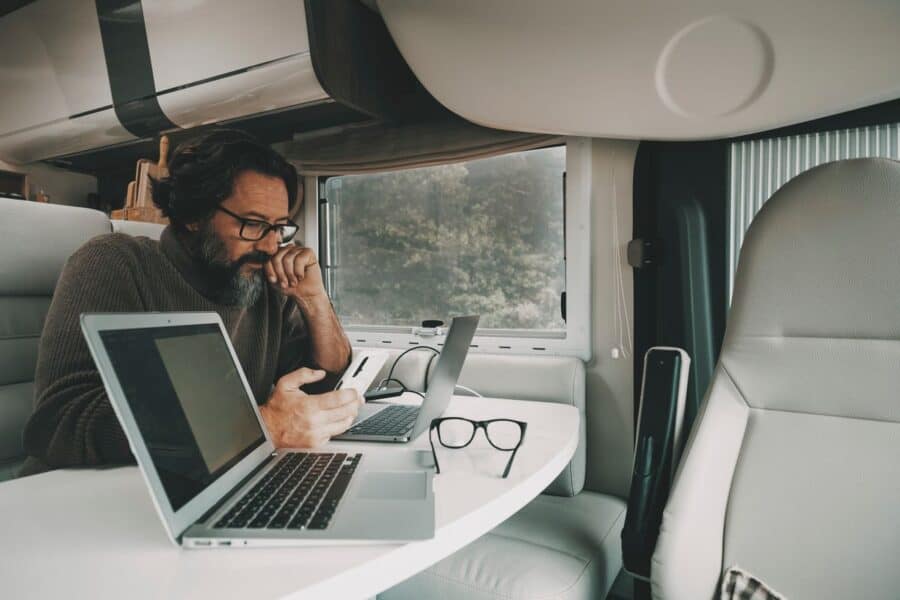 Man working on laptops inside a motorhome, using a smartphone, showcasing staying connected while exploring Europe.