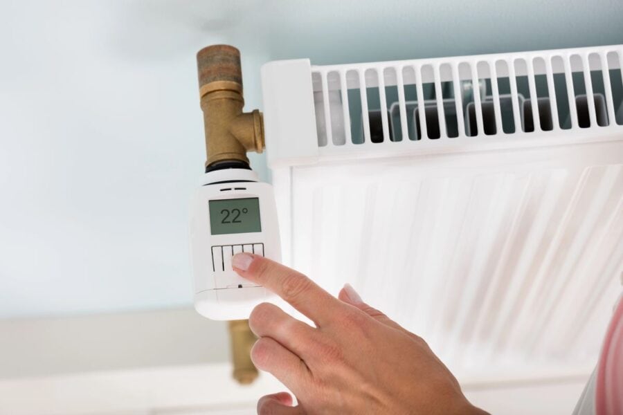 A person adjusting a radiator thermostat set to 22 degrees Celsius, demonstrating a way to control home heating for optimal warmth and energy efficiency.