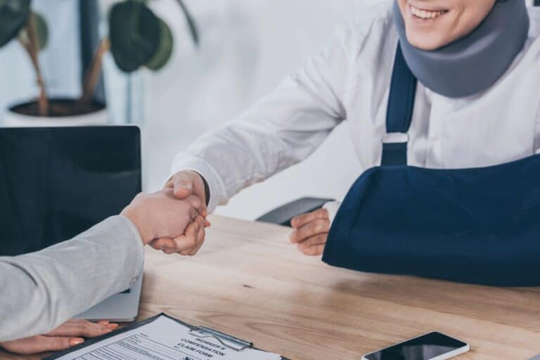 A person with a neck brace and arm sling shaking hands over a workers' compensation claim form, illustrating recovery and resolution after an unexpected injury in a public place.