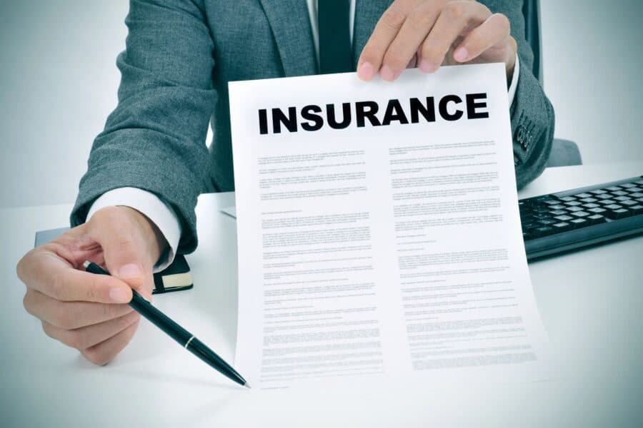 A professional in a suit holding an insurance document and a pen, suggesting upgrading house insurance during renovations.