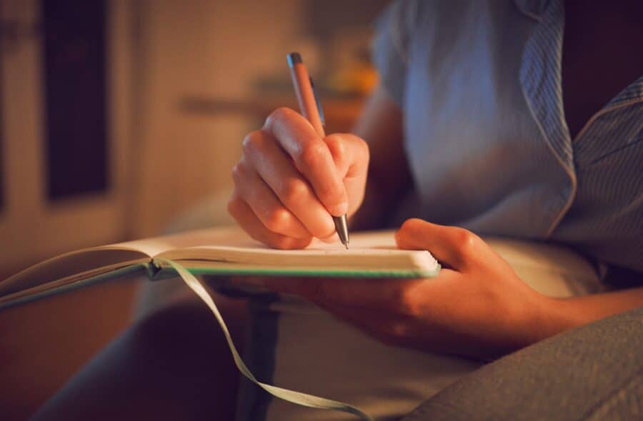 Close-up of a woman writing in a journal at night, practicing a calming bedtime ritual as part of self-care habits for busy parents.