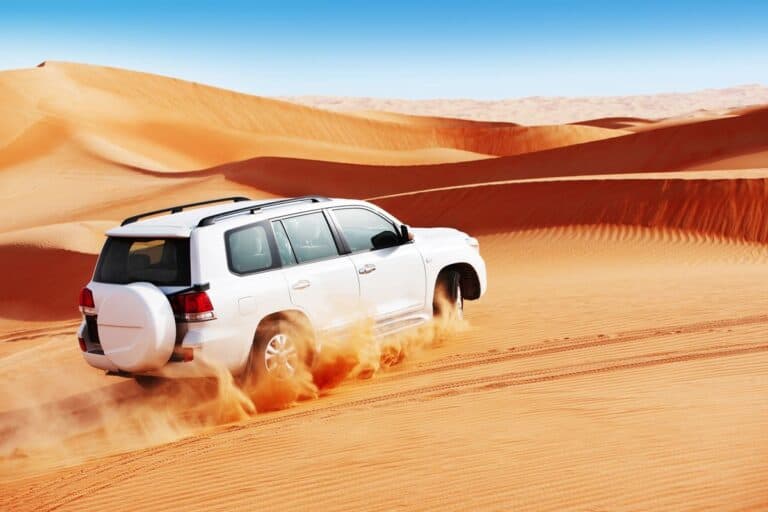 White SUV navigating through the golden desert dunes during thrilling driving adventures in Dubai.