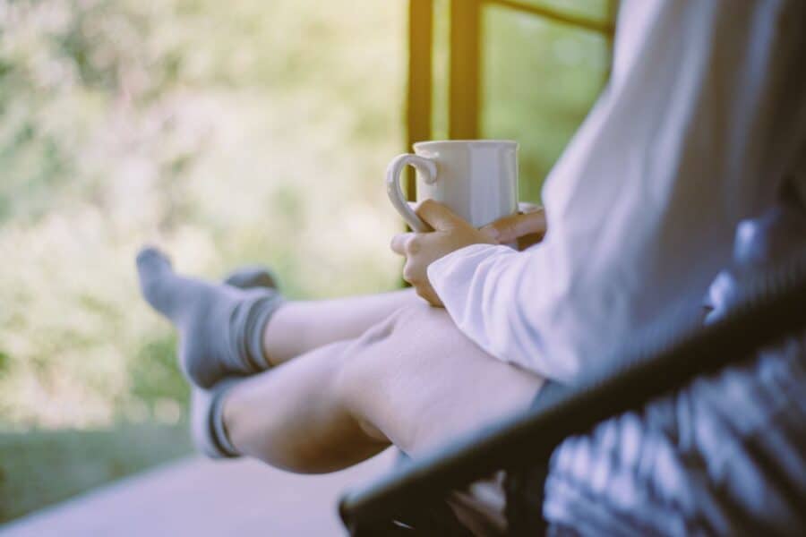 Person relaxing on a chair outdoors with a cup of tea, embracing peaceful self-care habits for busy parents to start the day.