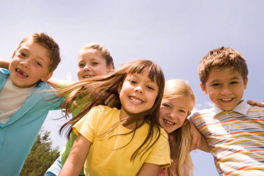 Group of happy children smiling outdoors under a clear blue sky.
