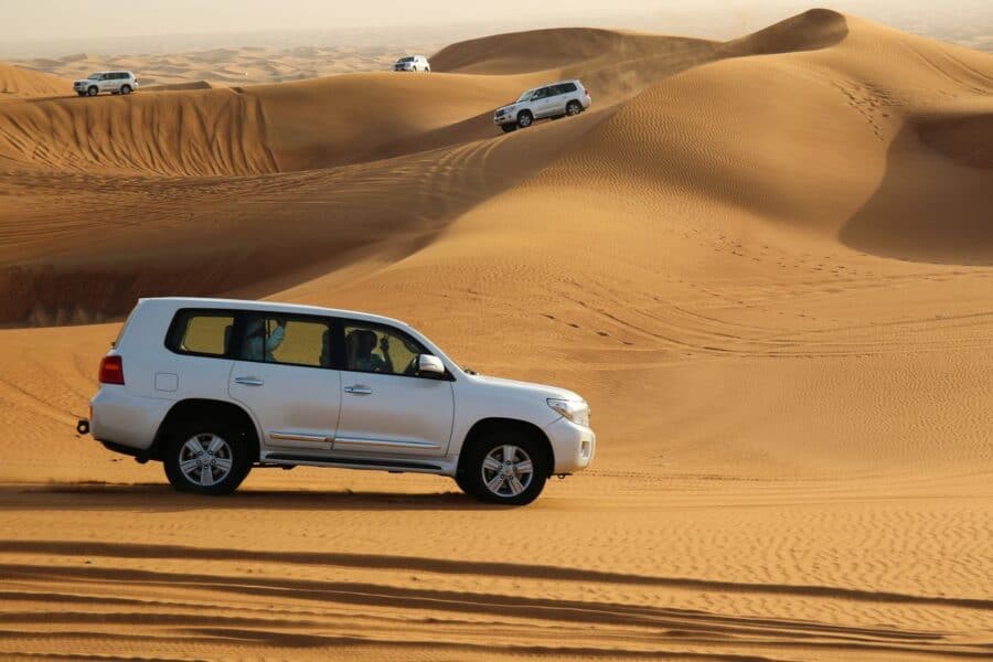 White SUVs driving across the golden sand dunes during exciting off-road driving adventures in Dubai.