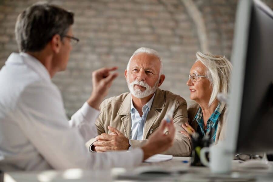 An older couple attentively listening to a doctor or advisor in a professional setting, reflecting the importance of health and financial planning in retirement.