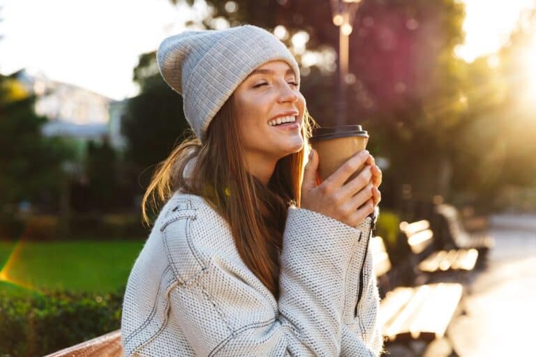 Smiling woman enjoying a warm drink outdoors on a sunny morning, embodying the essence of quick wellness breaks.