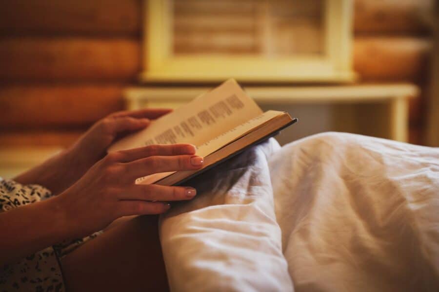 Hands holding an open book in a cosy bed, symbolising a calming evening routine with quick wellness breaks.