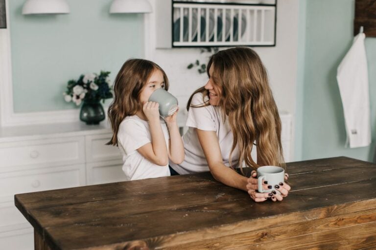 Mother and daughter smiling together in the kitchen, enjoying tea time as part of self-care habits for busy parents.