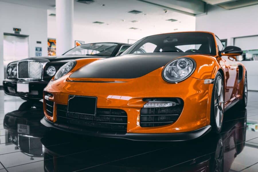 Luxury sports cars like Porsche and Bentley available for renting a car in Dubai, displayed in a sleek showroom.