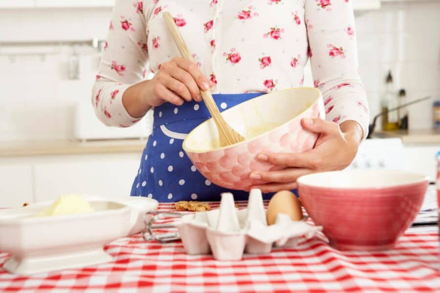Person in a floral top and polka dot apron mixing cake batter in a pink bowl.