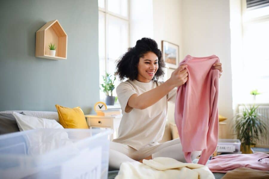 A cheerful woman organising clothes at home, demonstrating how decluttering your space can enhance your mood.