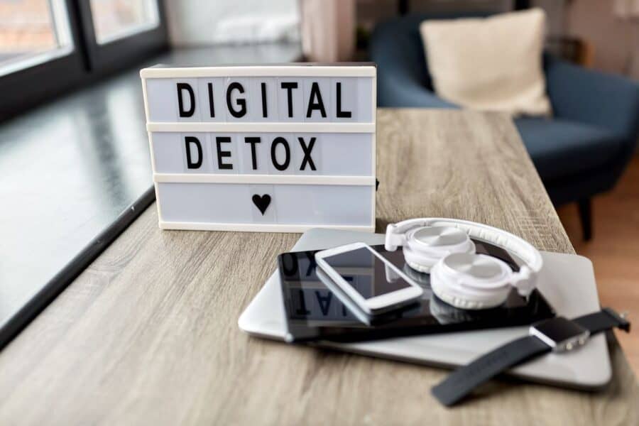 A desk with a sign displaying 'Digital Detox' next to headphones, a smartphone, tablet, and smartwatch.