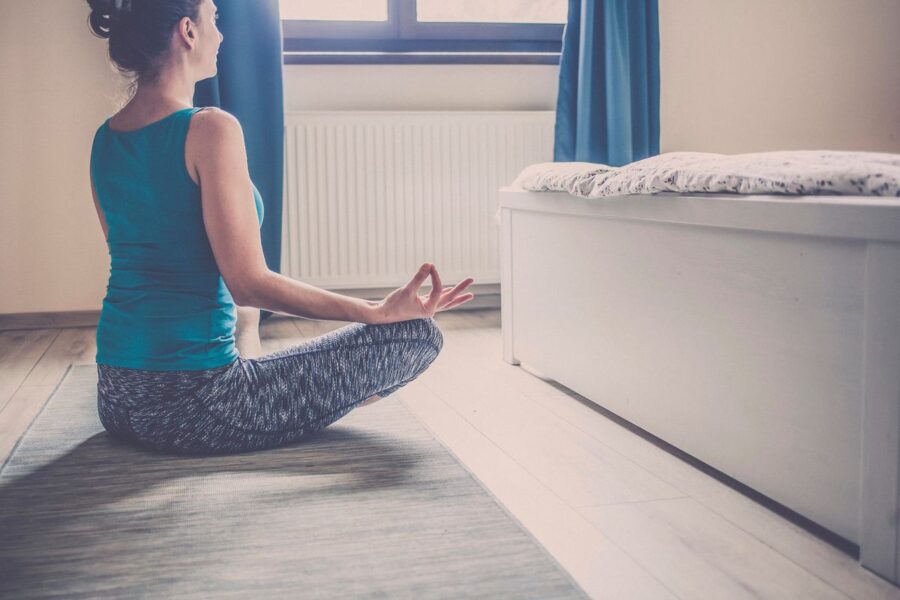 A woman sitting cross-legged on a yoga mat practicing a meditative pose in a peaceful, softly lit room.
