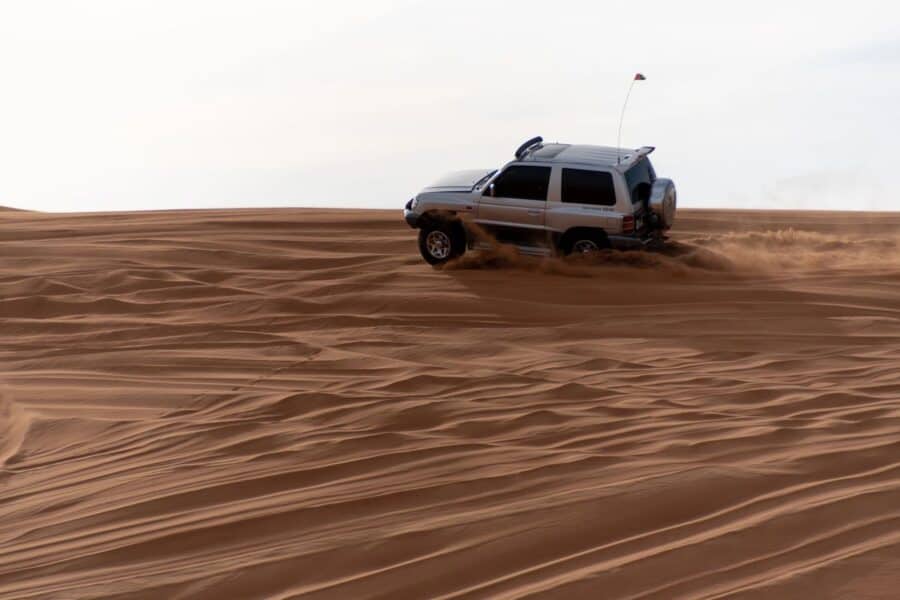Renting a car in Dubai: A luxury SUV driving on a scenic desert road under a clear blue sky.