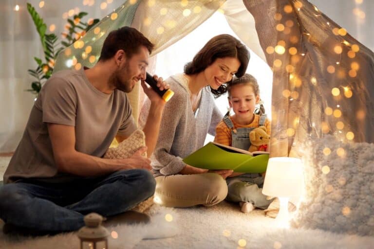 Family enjoying no-prep indoor activities with a cosy blanket fort, fairy lights, and a storytelling session using a flashlight.