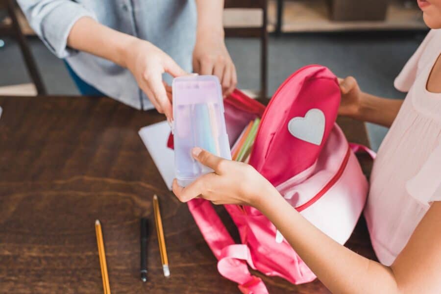 A parent and child packing a pink backpack with school supplies as part of their Sunday evening routine.
