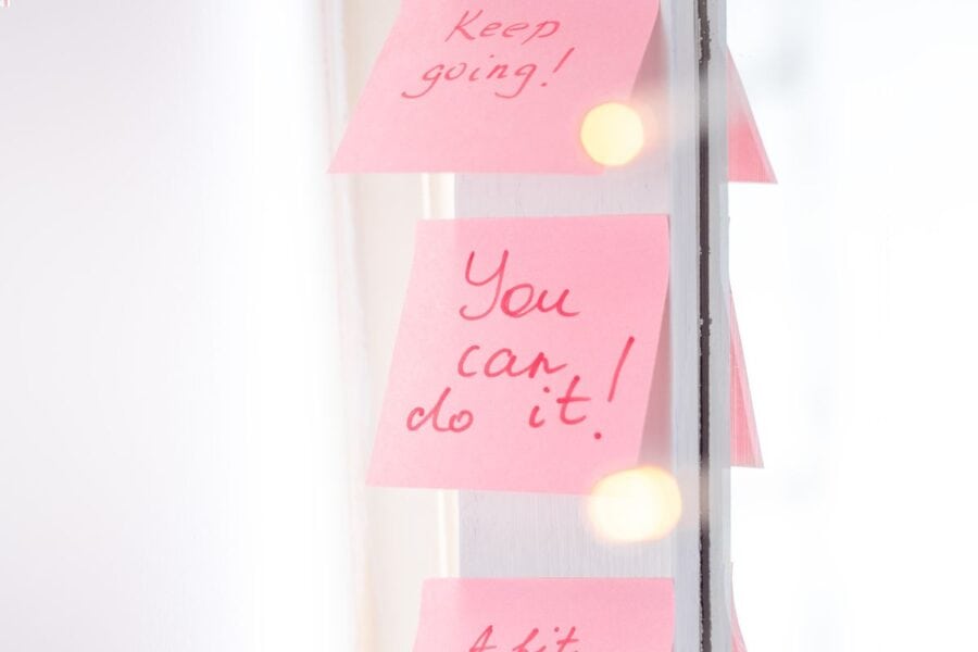 Pink sticky notes with motivational phrases like "You can do it!" and "Keep going!" stuck on a reflective surface, inspiring positive action and preparation.