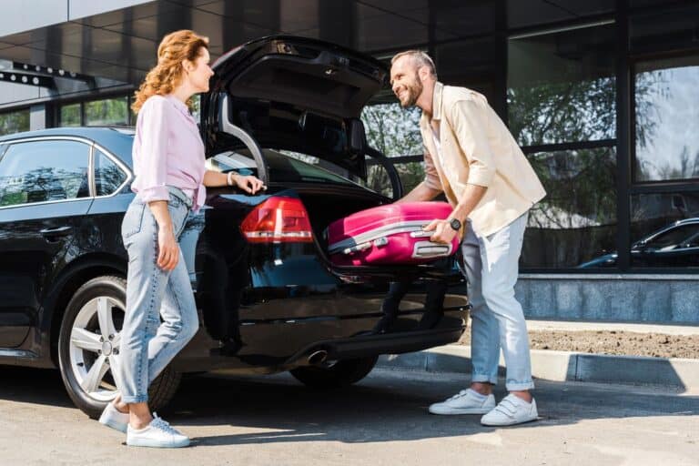 A couple of holidaymakers renting a car in Dubai and packing a red suitcase in the back of the car.