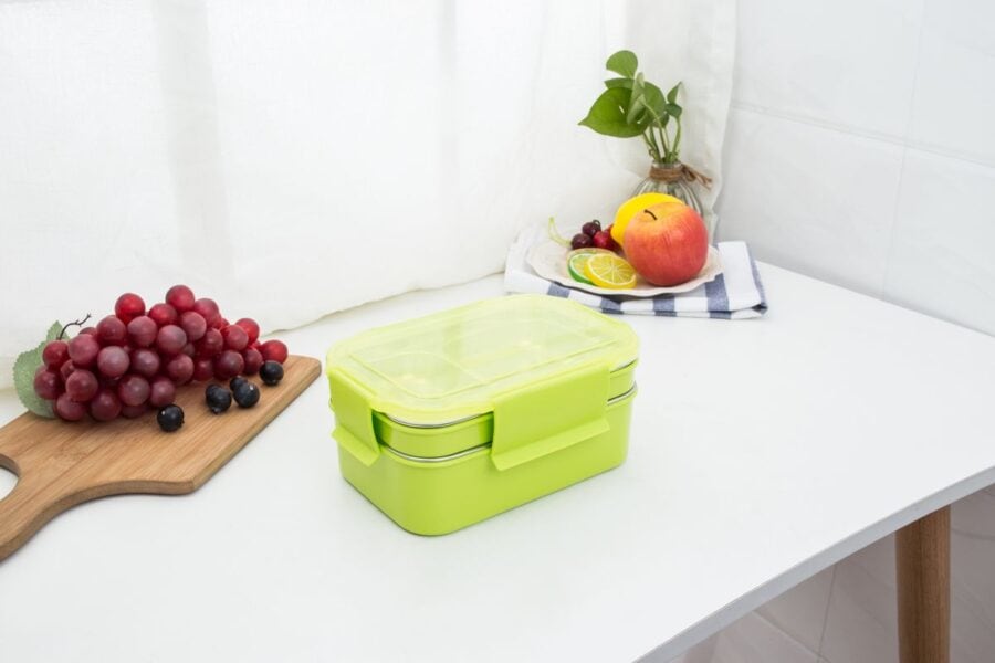 A clean kitchen counter with a green lunchbox packed and fresh fruits neatly arranged.