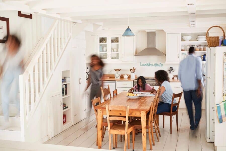 A busy family kitchen with children at the table and parents rushing around, preparing for the day ahead.