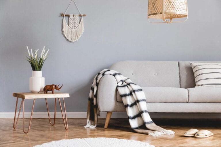 A cosy living room featuring a light grey sofa, striped cushions, a patterned throw, and a wooden side table, perfect to turn your home into a stylish escape.