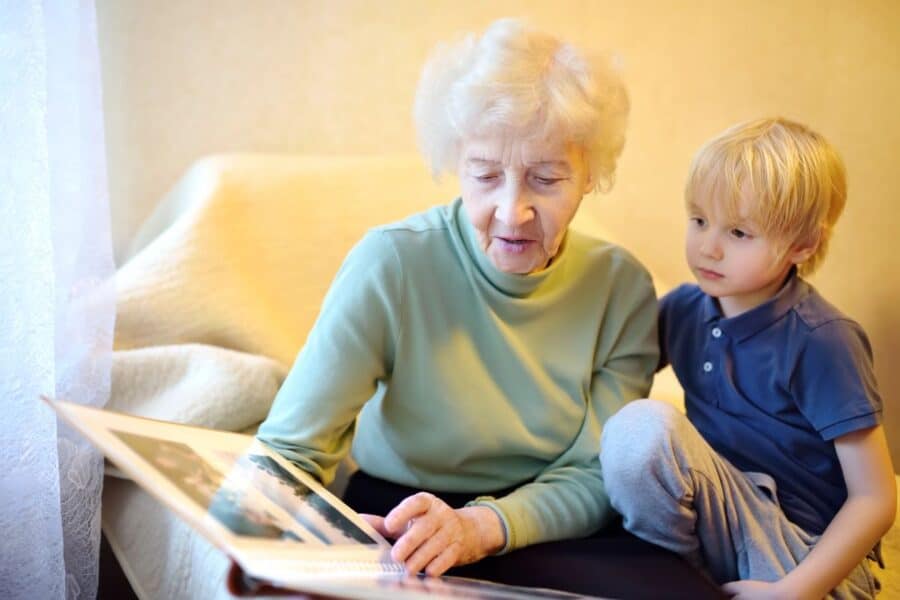 An elderly woman sharing a family photo album with her young grandchild, symbolising the importance of preserving family history and deepening family connections.