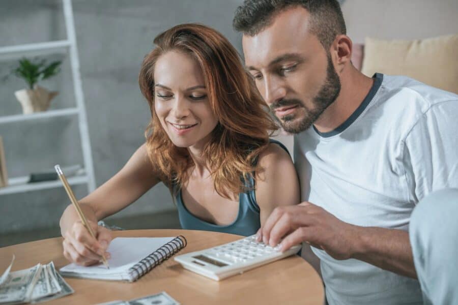 Young couple planning finances and future goals together, using a calculator and writing in a notebook.