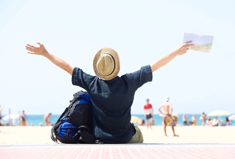 Man sitting on the beach with arms wide open, holding a map, symbolising freedom, goal-setting and life planning in his 30s.