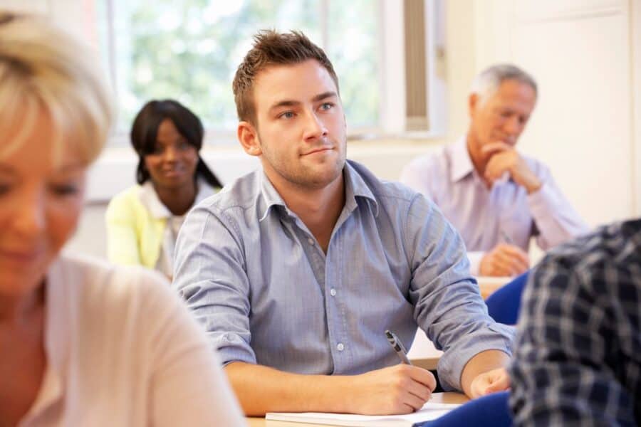 Young man attentively taking notes in a classroom, representing lifelong learning and personal growth in his 30s.