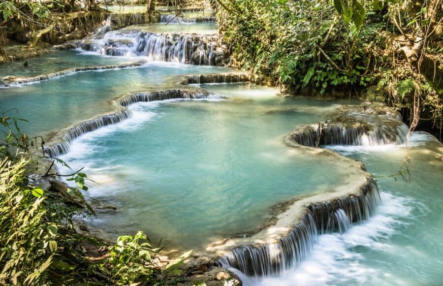 The turquoise cascading pools of Kuang Si Waterfalls, surrounded by lush green forest near Luang Prabang, Laos.