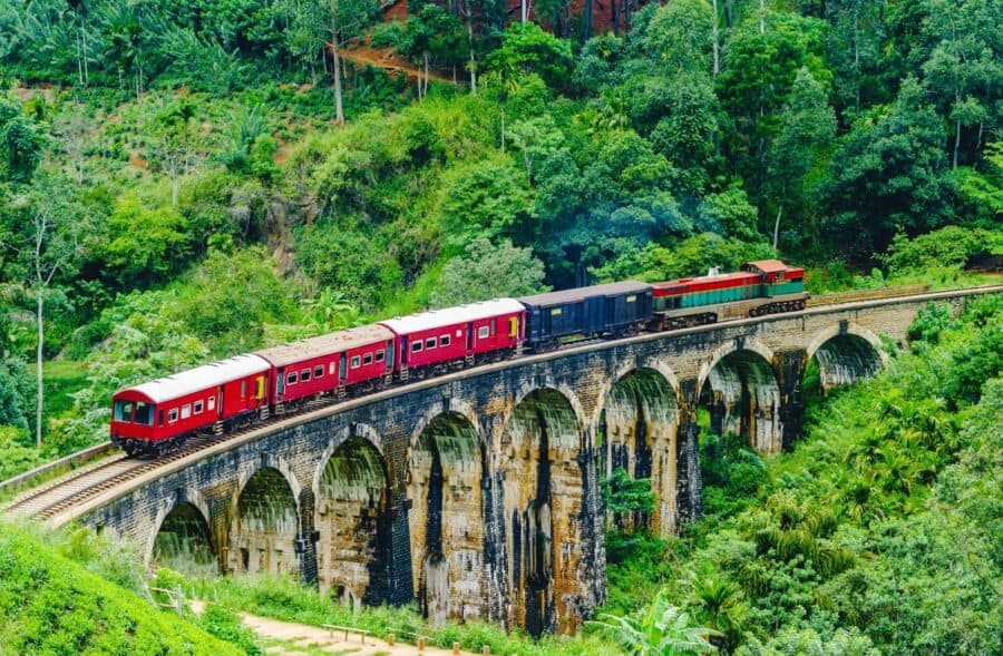 A red train crossing the iconic Nine Arches Bridge, one of the many unique destinations in Asia, surrounded by lush green hills in Ella, Sri Lanka.