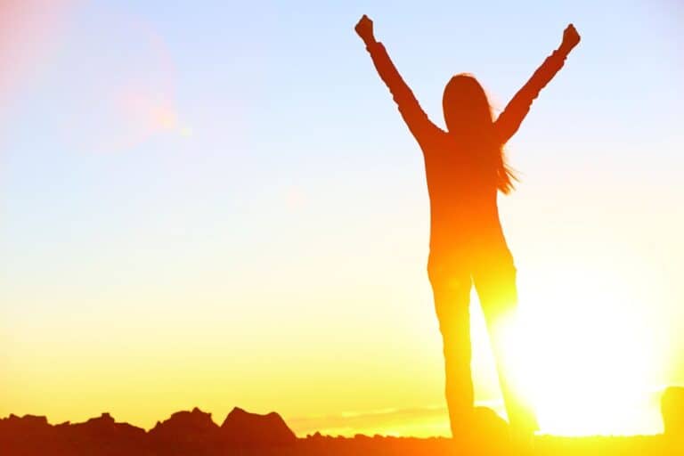 Silhouette of a woman standing on a mountain with arms raised at sunrise, symbolising success, motivation and planning in your 30s.