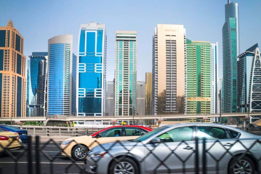 Modern skyscrapers in Dubai with cars driving on the highway, representing essential road trip car rental tips for exploring the UAE.