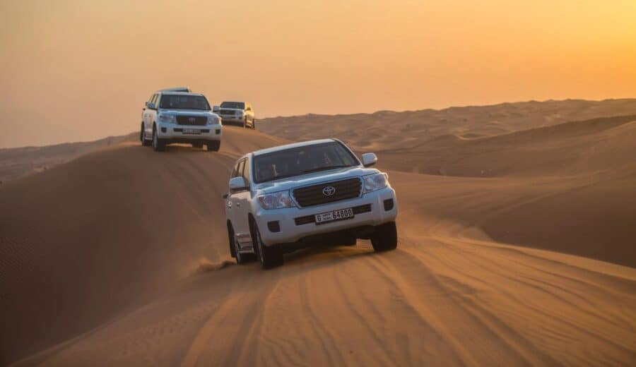 Convoy of 4x4 SUVs driving over sand dunes in the UAE desert at sunset, for off-road adventures.