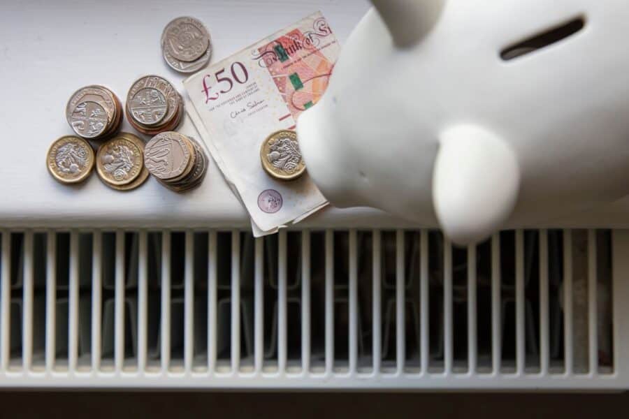 Piggy bank with UK pound coins and a £50 note placed on a radiator, symbolising savings from smart electrical upgrades.