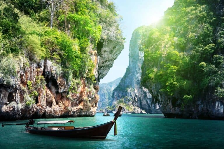 A traditional wooden long-tail boat floating on turquoise waters between towering limestone cliffs, representing unique holiday destinations in Asia.