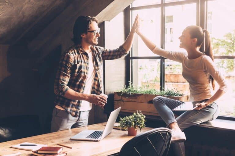 Two professionals celebrating a success with a high-five, demonstrating why accountability matters for staying on track with goals.