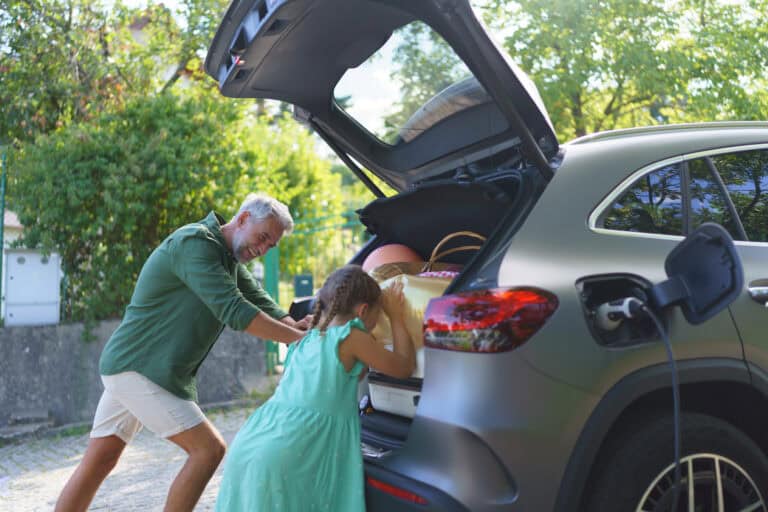 A family loading luggage into the trunk of an electric car lease for families while the vehicle is charging, showcasing the practicality of EVs.