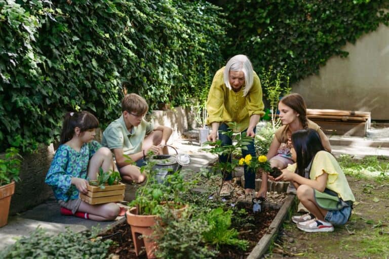 An elderly woman teaching children how to plant flowers and herbs in a garden, helping to encourage children to embrace sustainable living.