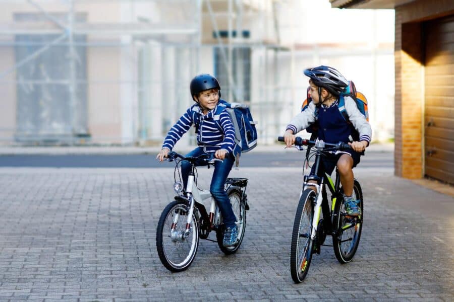 Two children riding bicycles to school, wearing backpacks and helmets, promoting sustainable transport and an active lifestyle.