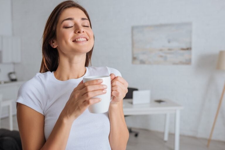 Woman pausing with eyes closed, holding a mug — a micro-moment of self-care and quick ways to find calm.