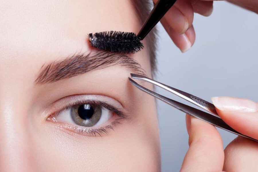Woman using a brush and pair of tweezers to help shape her eyebrows.